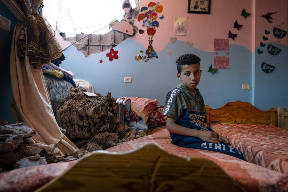 Ibrahim Al-Masri, 10, sits for a portrait in his bedroom that was damaged when an airstrike destroyed the neighboring building prior to a cease-fire that halted an 11-day war between Gaza's Hamas rulers and Israel, Wednesday, May 26, 2021, in Beit Hanoun, Gaza Strip. (AP Photo/John Minchillo)