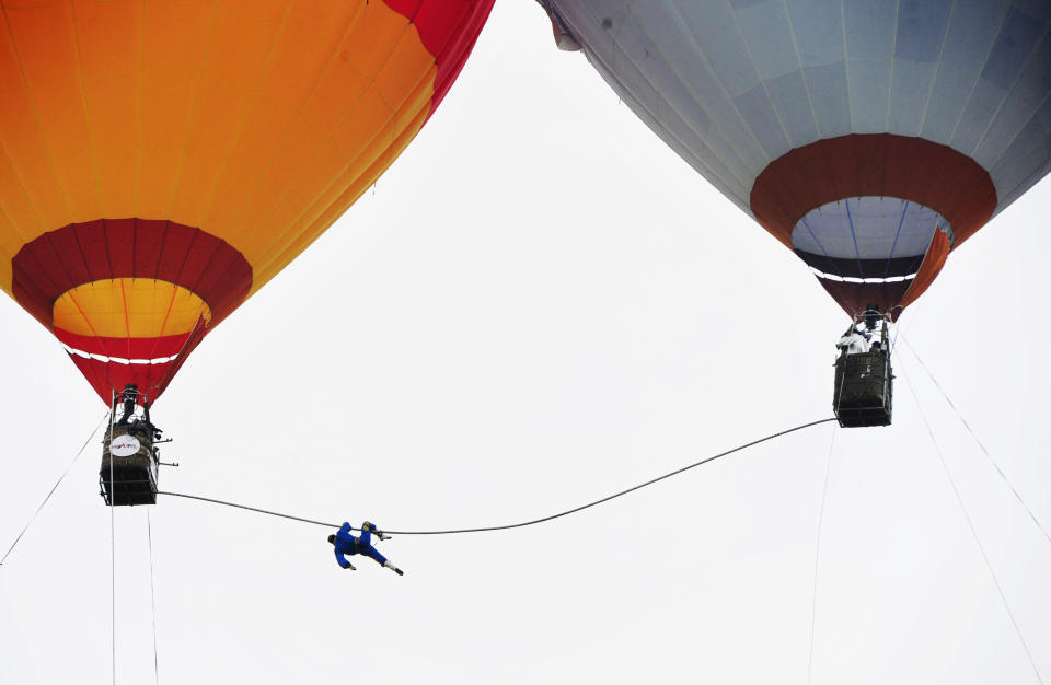 Saimaiti Aishan, a 27-year-old Uighur acrobat of tightrope walking, hangs on a 15-metre-long tightrope connected between two hot air balloons as he fails in an attempt for setting a 100 metre height record in Langshan, Hunan province August 6, 2011. Aishan, the nephew of Adili Wuxor, who is known as "Prince of the Tightrope", is the first person to perform tightrope walking between two hot air balloons. He set a national tightrope walking record at 30 metres high on Saturday, but failed in his attempt of 100 metres, local media reported. Picture taken August 6, 2011. REUTERS/China Daily