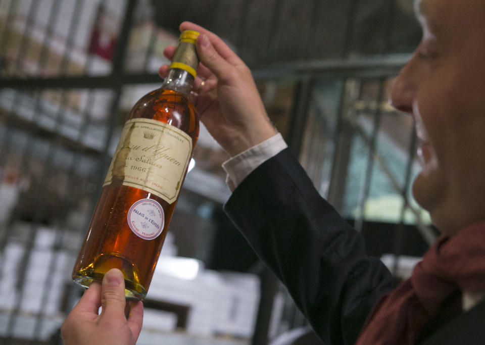 In this photo dated Tuesday May 28, 2013, an unidentified auction goer displays a bottle of 1966 Chateau d'Yquem premier cru Sauternes put on auction by the French presidential Palace during an auction preview in Issy les Moulineaux, south of Paris, France. French President Francois Hollande’s palace has decided to dive into its wine cellar and sell some of its treasures, to raise money and replenish its collection with more modest vintages. About 1,200 bottles, a tenth of the Elysee’s wine collection, are to be sold at Drouot auction house in Paris on Thursday and Friday. Organizers say that prices may reach up to 2,200-2,500 euros for a 1990 Petrus down to 15 euros for a more modest wine. (AP Photo/Jacques Brinon)