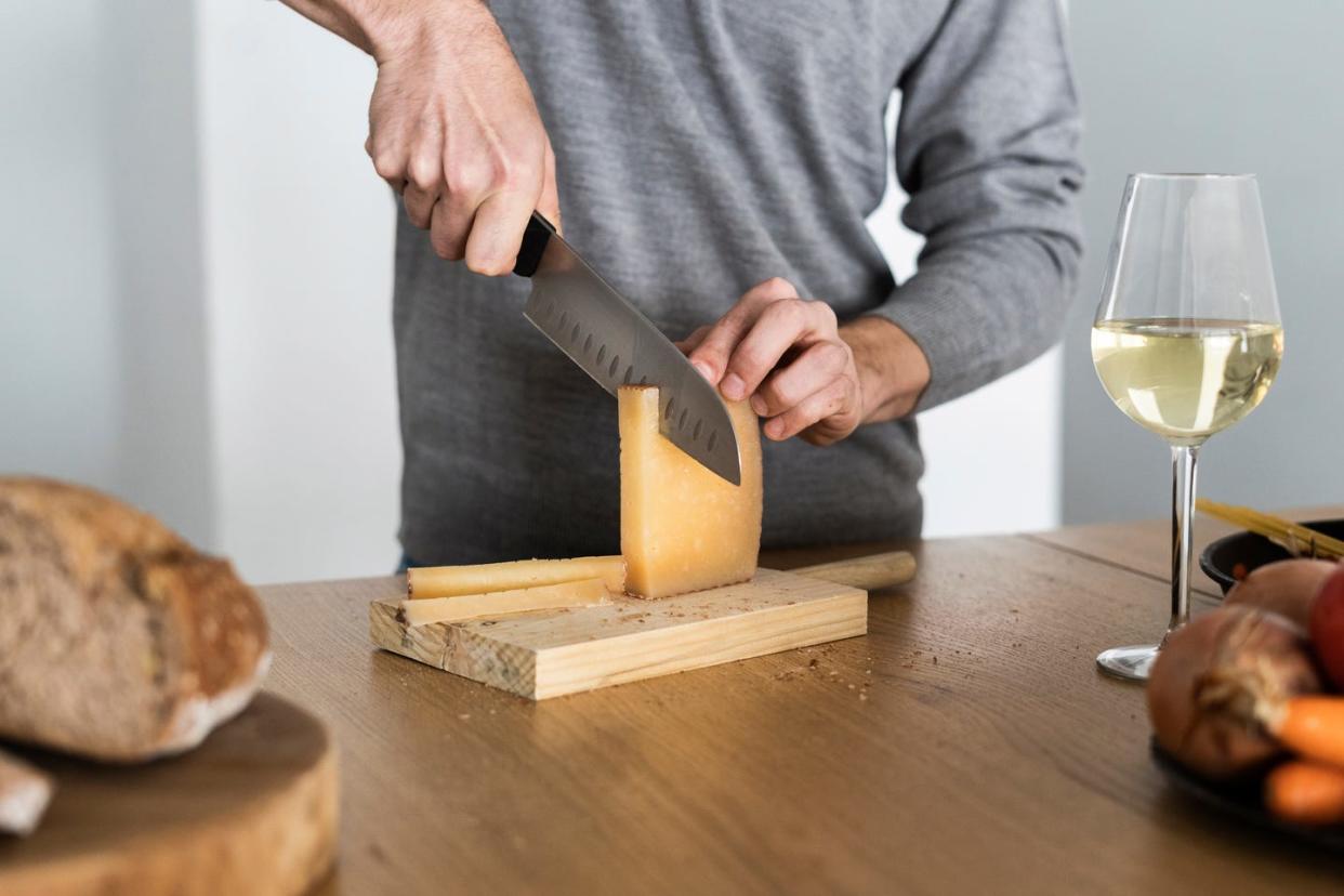 Close-up of a man cutting cheese at kitchen counter