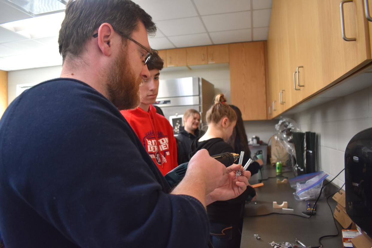 Thomas Buxton, treasurer for the Rotary Club of Tecumseh, shows the process of embossing and sealing a small tube with heat Thursday, March 21, 2024, to Britton Deerfield junior Ryan Good who is a student enrolled in the Agri-Tech program at the Lenawee Intermediate School District (LISD) Tech Center. The Rotary Club of Tecumseh and students from the Tech Center's FFA program worked together last week on creating reusable Water Pasteurization Indicators, known by the acronym WAPI.