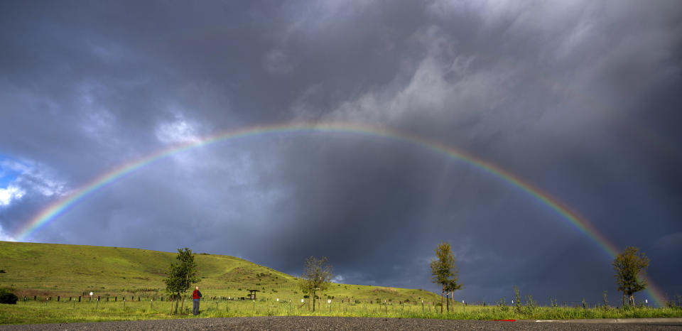 Adwait Bhagwat, of Irvine, stops to photograph a full rainbow seen over a meadow near the Interstate 405 freeway in Irvine, Calif., Sunday, March 31, 2024. Bhagwat, an amatuer photographer, said he is always looking to capture "natural phenomena." Next week he plans to travel to Texas to view the eclipse. (Mindy Schauer/The Orange County Register via AP)