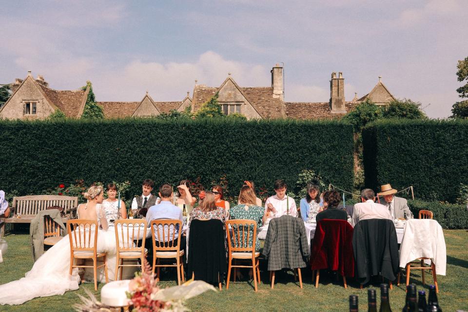 A group of people sits at an outdoor table in a garden.