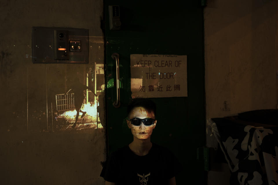 In this Oct. 19, 2019, photo, a protester who identified himself as Eliot, 33, poses for a portrait as a projector displays a photograph, previously taken during the unrest, over him at a protest in Hong Kong. Eliot believes that his role in the protest is to protect the younger demonstrators, "If it's necessary I can be arrested for them" he says. (AP Photo/Felipe Dana)