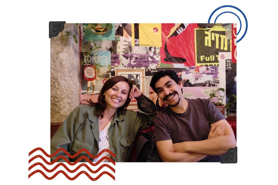 A smiling woman and man lean in for a photo in front of a wall of posters.