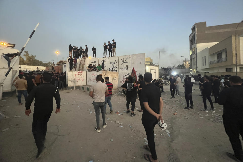 CORRECTS SECOND SENTENCE - Protesters scale a wall at the Swedish Embassy in Baghdad Thursday, July 20, 2023. Protesters angered by the planned burning of a copy of the Quran stormed the embassy early Thursday, breaking into the compound and lighting a small fire. (AP Photo/Ali Jabar)