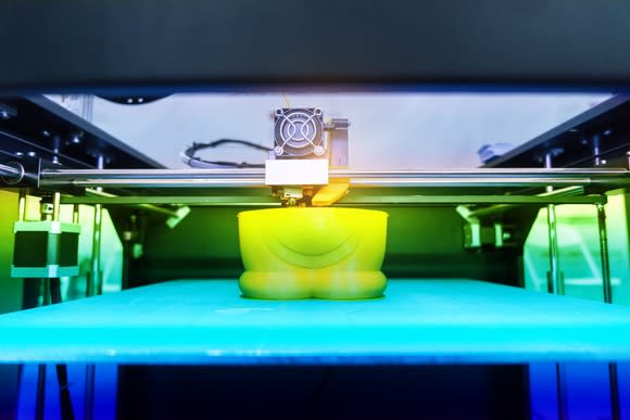 Close-up of a 3D printer printing a yellow plastic object.