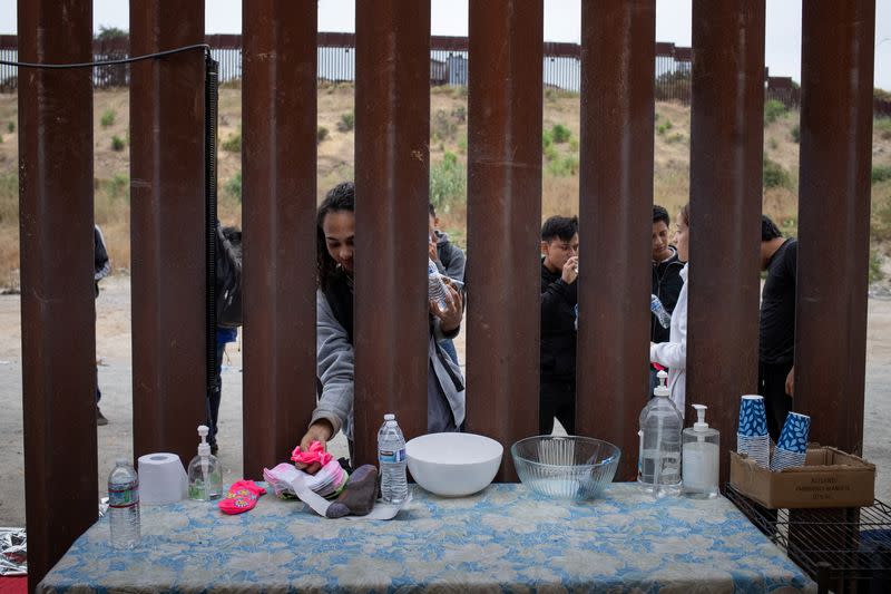 Migrant grabs donated water and supplies between border walls in San Diego