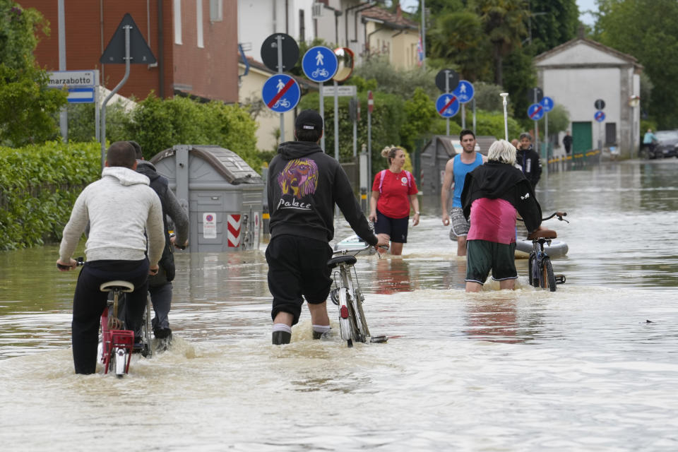 People pedal in a flooded street in Barbiano di Cotignola, Italy, Thursday, May 18, 2023. Exceptional rains Wednesday in a drought-struck region of northern Italy swelled rivers over their banks, killing at least nine people. Rescue crews worked Thursday to reach isolated towns and villages in northern Italy that were cut off from highways, electricity and cellphone service following heavy rains and flooding, as farmers warned of "incalculable" losses and authorities began mapping out cleanup and reconstruction plans. (AP Photo/Luca Bruno)