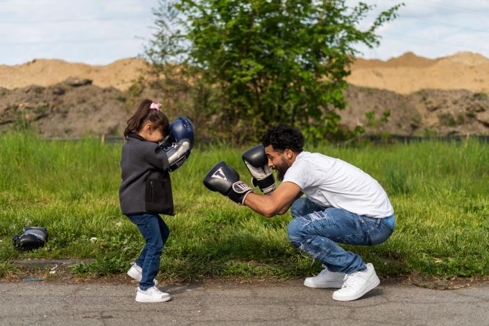 Dwayne Taylor, of Lincoln Park, puts on boxing gloves as his daughter Niyah Taylor looks to challenge him while waiting for people to show up for the start of a Pick Your Poison Detroit boxing event run by Taylor in Detroit&#39;s Delray neighborhood on Sunday, May 16, 2021.