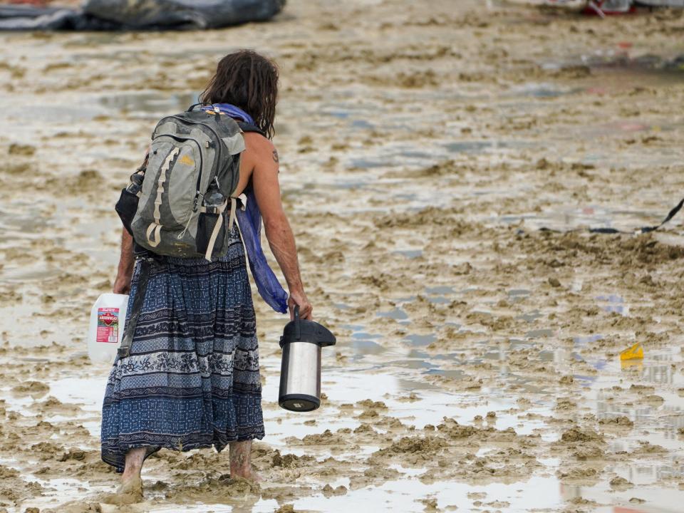 A festival-goer walks through mud, carrying a backpack.