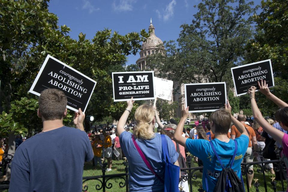 Four people face away from the camera holding up signs that read 'Courageously Abolishing Abortion'