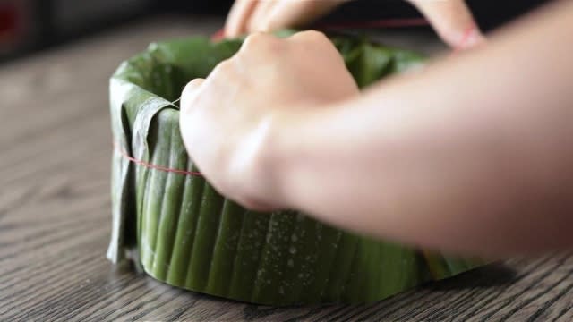 Tying rubber band around banana leaves wrapped around baking tin