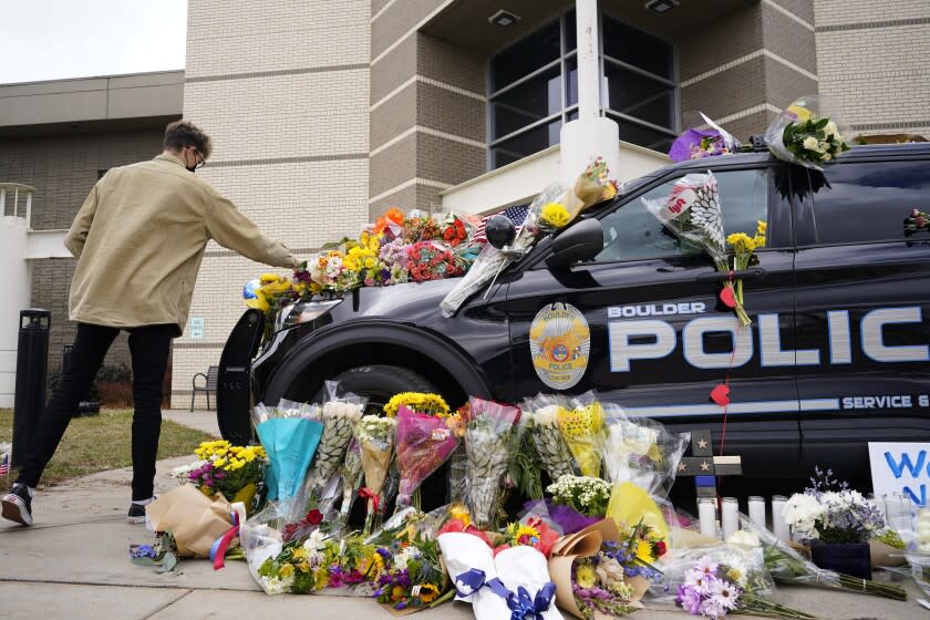 In this March 23, 2021, photo, a man leaves a bouquet on a police cruiser parked outside the Boulder Police Department after an officer was one of the victims of a mass shooting at a King Soopers grocery store in Boulder, Colo. The suspects in the most recent shooting sprees found it relatively easy to get their guns. The suspect in the shooting at a Boulder supermarket was convicted of assaulting a high school classmate but still got a gun.(AP Photo/David Zalubowski)