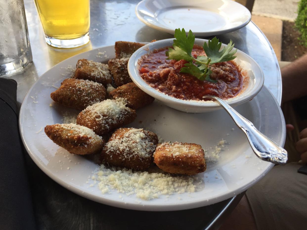 Toasted ravioli sprinkled with parmesan cheese with marinara sauce garnished with parsley on a white plate at an Italian restaurant on The Hill in St. Louis, Missouri, USA.