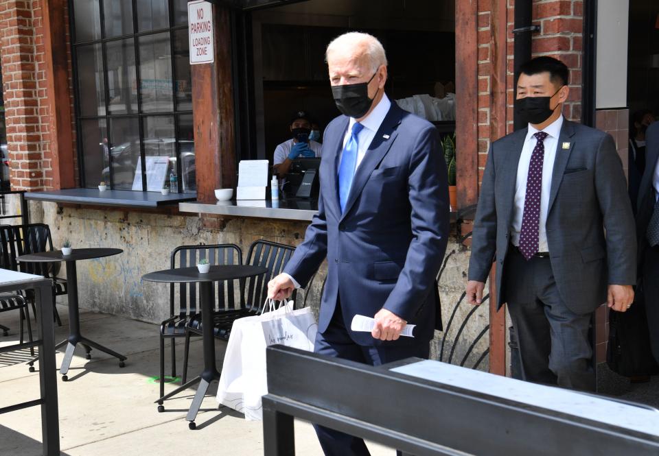 President Biden, wearing a black face mask, leaves a restaurant holding white paper bags