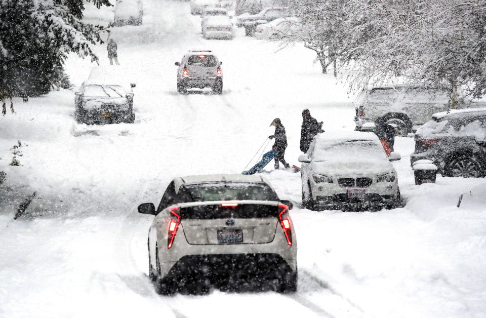 A sledder moves aside as traffic heads downhill in heavy snow falling Monday, Feb. 11, 2019, in Seattle. Schools closed across Washington state and the Legislature canceled all hearings Monday with winter snowstorms pummeling the Northwest again as a larger weather system wreaked havoc in the region and even brought snow to Hawaii. (AP Photo/Elaine Thompson)