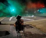 A protester sits while riot police fire tear gas in his direction during nationwide unrest following the death in Minneapolis police custody of George Floyd, in Raleigh