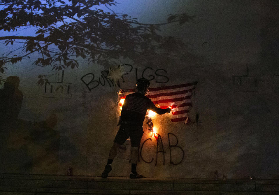 FILE - In this July 4, 2020, file photo, protesters burn a U.S. flag in downtown Portland, Ore. The U.S. Attorney in Oregon announced federal charges Tuesday, July 7, against seven protesters who are accused in court papers of defacing a federal courthouse and assaulting federal officers during protests in Portland, Oregon against racial injustice and police brutality. The protesters are charged with offenses ranging from disorderly conduct to destruction of federal property and assaulting a federal officer and were released pending trial after a brief court hearing Monday. (Beth Nakamura/The Oregonian via AP, File)