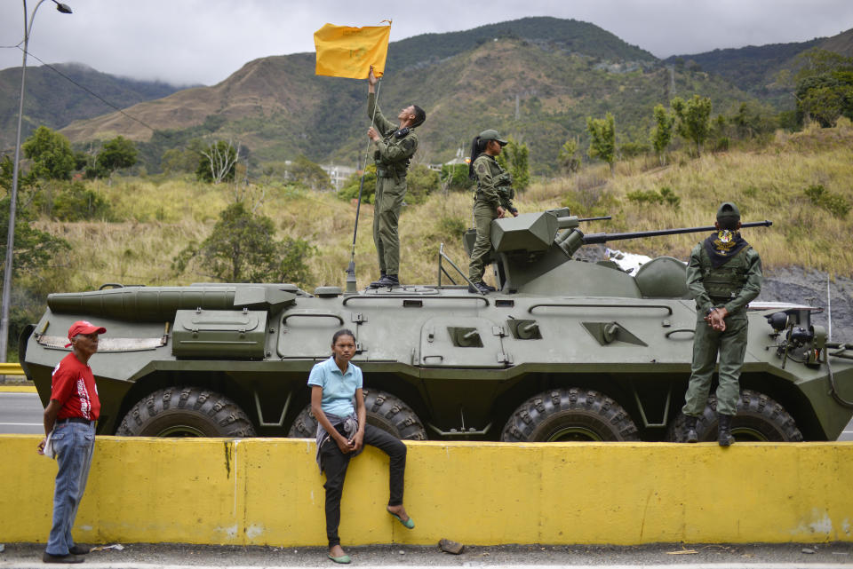 A woman sits next to an armored vehicle taking part in military exercises in Caracas, Venezuela, Saturday, Feb. 15, 2020. Venezuela's President Nicolas Maduro ordered two days of nationwide military drills, including the participation of civilian militias. (AP Photo/Matias Delacroix)