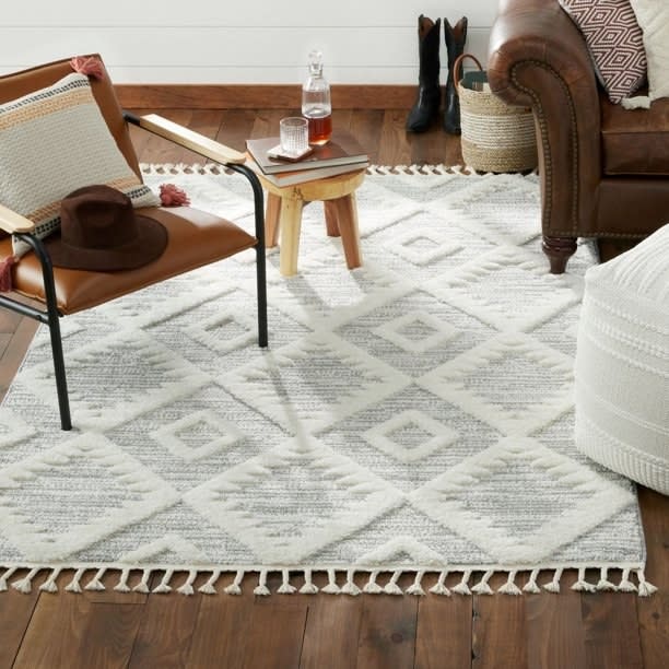 Geometric patterned rug in a living area with an accent chair, side table with glass, leather armchair, and boots
