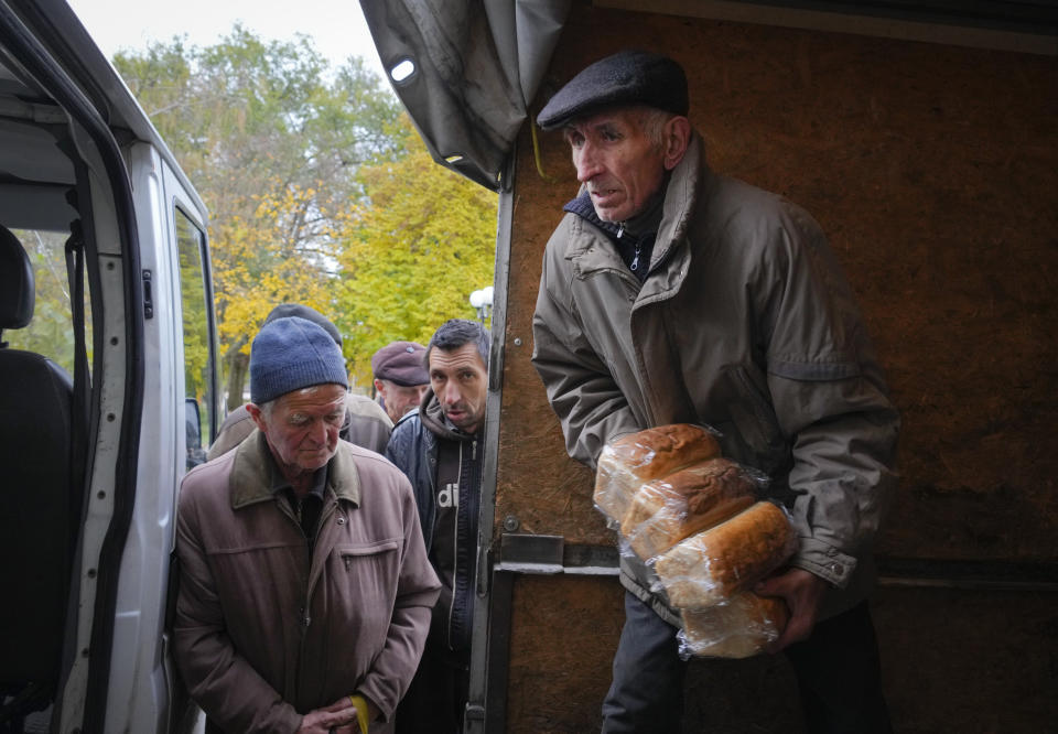 A volunteer unload bread as local residents wait for free bread distribution in Bakhmut, the site of the heaviest battle against the Russian troops in the Donetsk region, Ukraine, Friday, Oct. 28, 2022. (AP Photo/Efrem Lukatsky)