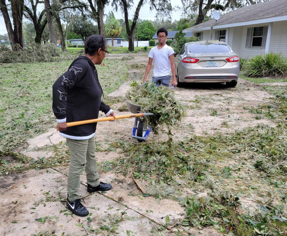 Renay Lee collects debris Thursday afternoon at her cousin's house in Bartow as a neighbor, Justin Knight, collects it in a wheelbarrow.