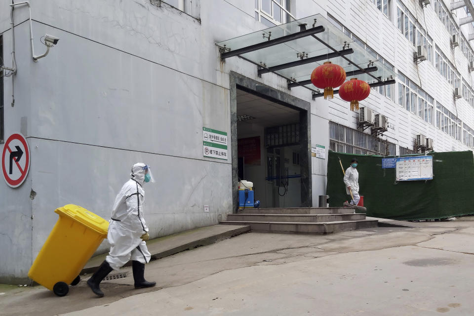 In this Thursday, Jan. 23, 2020, photo, a staff member wearing a hazardous materials suit hauls a bin at a hospital that reported a coronavirus death in Yichang in central China's Hubei Province. China is swiftly building a 1,000-bed hospital dedicated to patients infected with a new virus that has killed 26 people, sickened hundreds and prompted unprecedented lockdowns of cities during the country's most important holiday. (Chinatopix via AP)