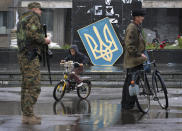 FILE - A boy rides a bike in the city of Slovyansk, Donetsk Region, eastern Ukraine Monday, July 7, 2014, with a Ukrainian state emblem in the background. (AP Photo/Dmitry Lovetsky, File)