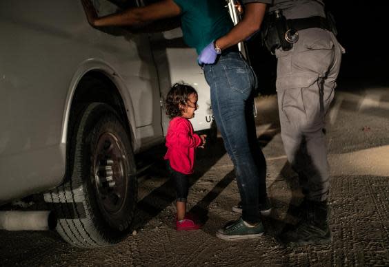 A two-year-old Honduran asylum seeker cries as her mother is searched and detained at the border (Getty)