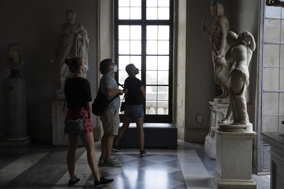 Visitors wearing a face masks to prevent the spread of COVID-19 admire statues in the Rome Capitoline Museums, including the second century A.D. Roman marble statue "Cupid and Psyche", at right, Tuesday, May 19, 2020. In Italy, museums were allowed to reopen this week for the first time since early March, but few were able to receive visitors immediately as management continued working to implement social distancing and hygiene measures, as well as reservation systems to stagger visits to museums in the onetime epicenter of the European pandemic. (AP Photo/Alessandra Tarantino)