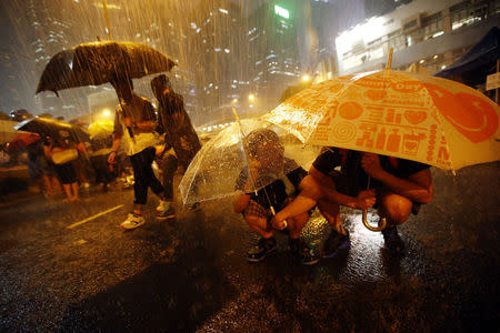 Protesters take shelter from the rain under umbrellas as they block the main street to the financial Central district outside of the government headquarters in Hong Kong, September 30, 2014. REUTERS/Carlos Barria