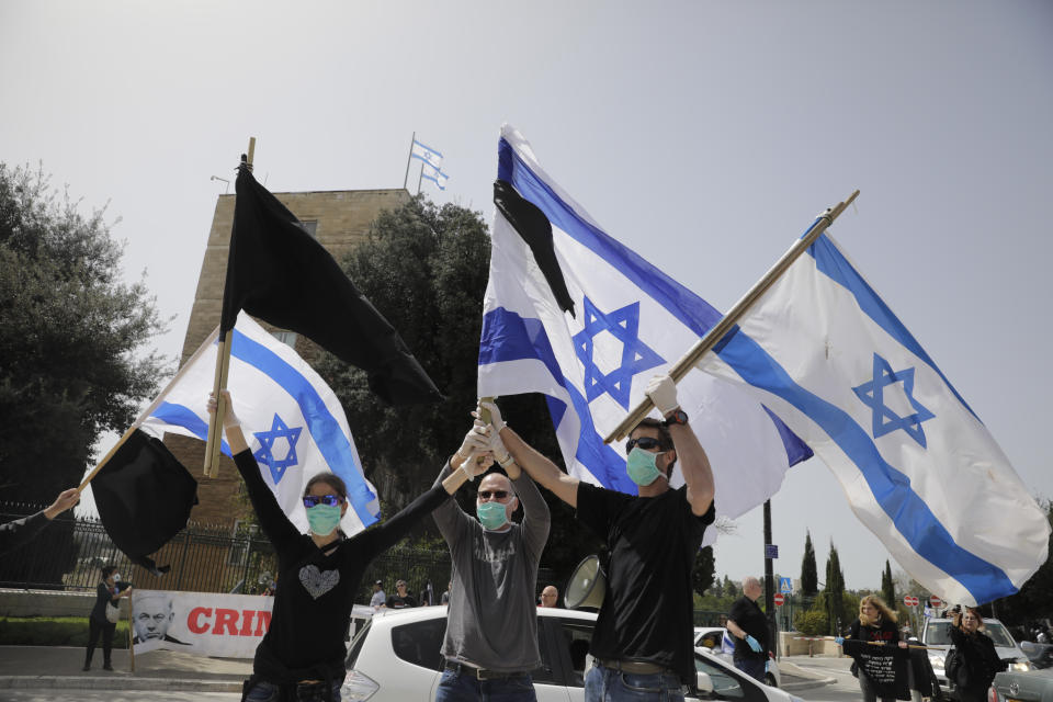 Israelis hold national flags during a protest against Prime Minister Benjamin Netanyahu outside the national parliament in Jerusalem, Monday, March 23, 2020. The opposition has accused Netanyahu of using the coronavirus crisis as cover to undermine the country's democratic institutions. With the country in near-shutdown mode, Netanyahu has already managed to postpone his own pending criminal trial and authorize unprecedented electronic surveillance of Israeli citizens. (AP Photo/Sebastian Scheiner)