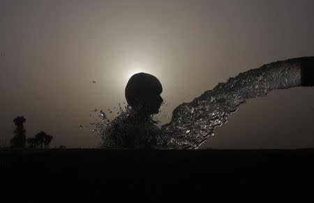 A boy is silhouetted against the setting sun as he cools himself off under a pipe during a hot day in Faisalabad on June 27, 2012. REUTERS/Fayyaz Hussain