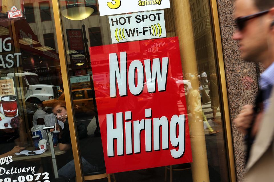 A "now hiring" sign is viewed in the window of a business.