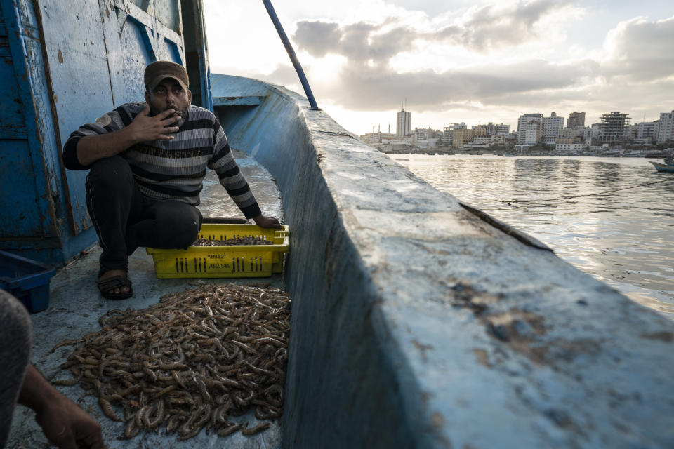 A fisherman takes a drag from his cigarette while sorting shrimp on deck after a limited number of boats are allowed to return to the sea following a cease-fire reached after an 11-day war between Gaza's Hamas rulers and Israel, in Gaza City, Sunday, May 23, 2021. (AP Photo/John Minchillo)