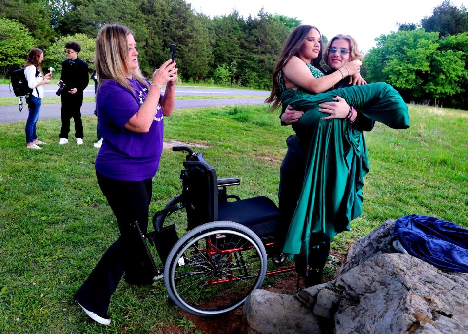 Tucker Moore lifts Janae Edmondson and places her back into her chair after taking pre-prom photos on a rock at The Stones River Battlefield on Saturday, April 29, 2023, before prom. Francine Edmondson the mother of Janae Edmondson takes photos as Lynette Knight and her son Tybee Phomthisene finish taking photos of the couple before prom. 