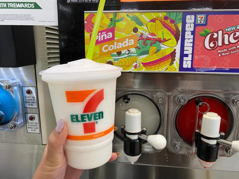 A hand filling up a large 7/11 cup with pina colada slurpee