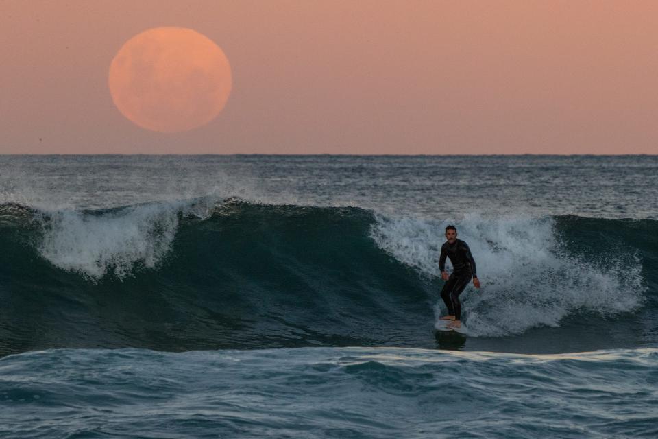 A surfer rides a wave as a super blood moon rises above the horizon at Manly Beach on May 26, 2021, in Sydney, Australia.