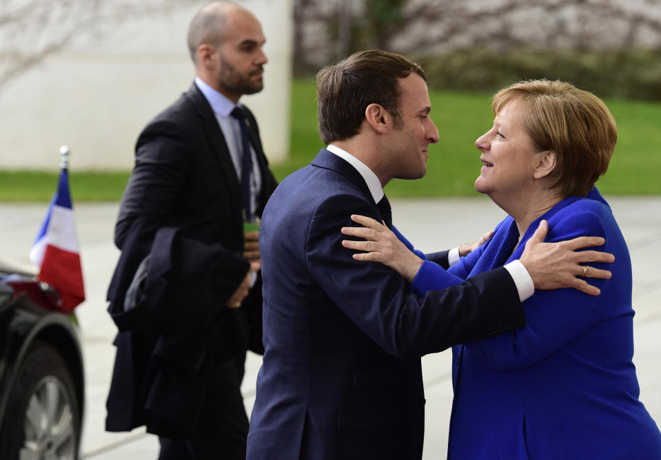 German Chancellor Angela Merkel, right, greets French President Emmanuel Macron, center, during arrivals for a conference on Libya at the chancellery in Berlin, Germany, Sunday, Jan. 19, 2020. German Chancellor Angela Merkel hosts the one-day conference of world powers on Sunday in Berlin to discuss efforts to broker peace in Libya. (AP Photo/Jens Meyer)