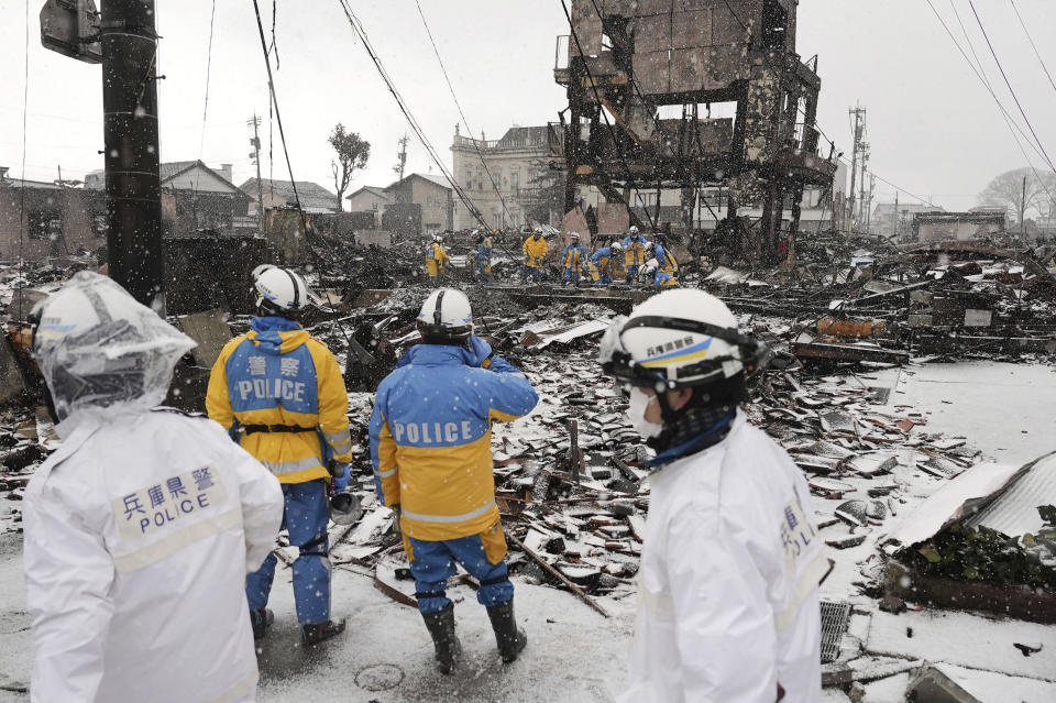 Snow falls as police officers continue a search operation around a burnt market in Wajima, Ishikawa prefecture, Japan Sunday, Jan. 7, 2024. A major earthquake slammed western Japan on Jan. 1, killing scores of people, toppling buildings and setting off landslides. (Kyodo News via AP)
