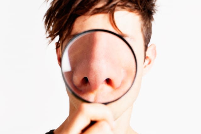 Cute but nerdy young man holds up a magnifying glass, enlarging his nose enormously - all the better to smell you with!