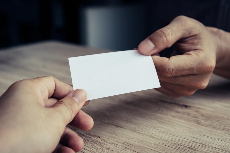 Two businessmen exchanged business cards on a wooden table. White business cards. Copy space.