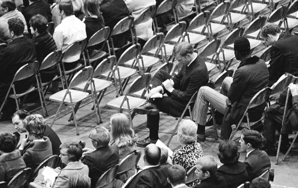 FILE - Marshall assistant football coach Red Dawson, center, sits alone during a memorial service at the Veterans Memorial Field House on Nov. 15, 1970, in Huntington, W.Va., honoring the 75 people killed in a plane crash. A bill has won final legislative approval Wednesday, Feb. 15, 2023, in West Virginia, that would establish an annual day of recognition for the worst sports disaster in U.S. history, a plane crash that killed most of Marshall University's football team. (Lee Bernard/The Herald-Dispatch via AP, File)