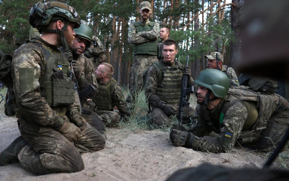 A group of Ukrainian soldiers in camouflage gear huddle together in a forest