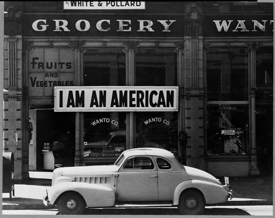 Sign stating "I AM AN AMERICAN" is hung in a storefront one day after Pearl Harbor