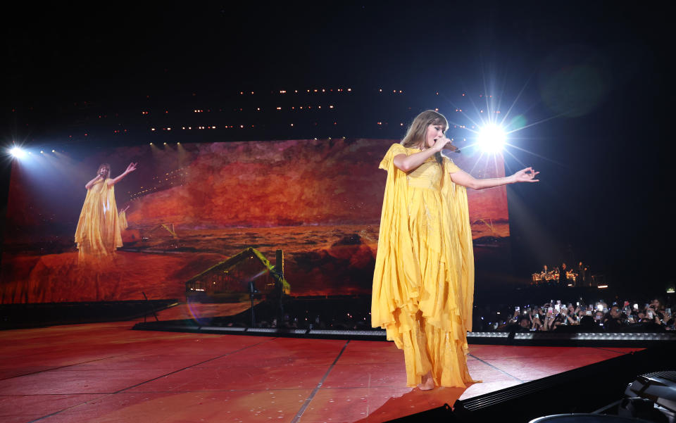 Taylor Swift, in a long yellow dress, sings onstage.