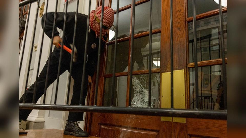 Masked person breaks door window with hammer