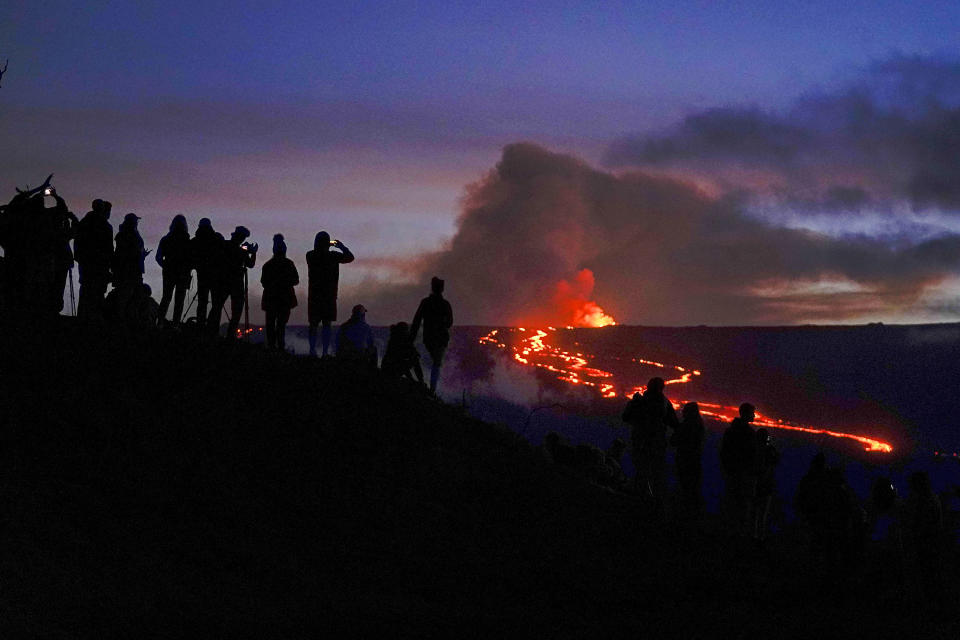 FILE - People watch and record images of lava from the Mauna Loa volcano Thursday, Dec. 1, 2022, near Hilo, Hawaii. Officials monitoring the Mauna Loa eruption on Hawaii's Big island said Wednesday, Dec. 7, the lava flow moving toward state Route 200 has slowed. They said they could not predict when, where or if the lava flow would cross the highway. (AP Photo/Gregory Bull, File)