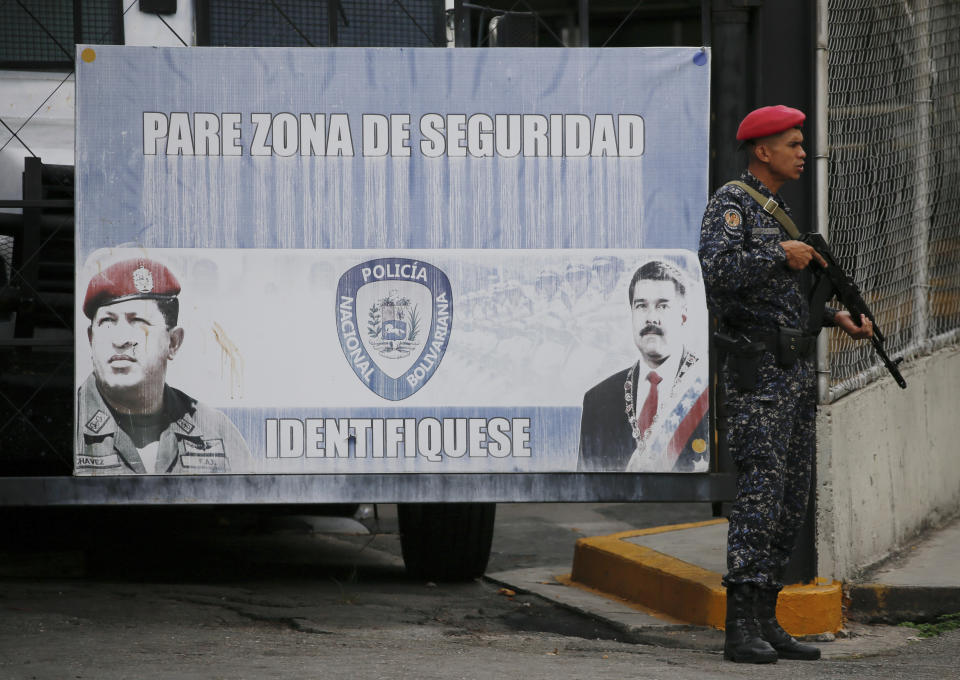 A Venezuelan Bolivarian National Police officer stands guard at the main entrance of the Helicoide prison in Caracas, Venezuela, Thursday, May 9, 2019, where Edgar Zambrano, vice president of the opposition-controlled National Assembly, is being held after his arrest. The sign in the background shows late President Hugo Chavez, left, current President Nicolas Maduro, and reads in Spanish: "Stop, security zone. Identify yourself." (AP Photo/Fernando Llano)